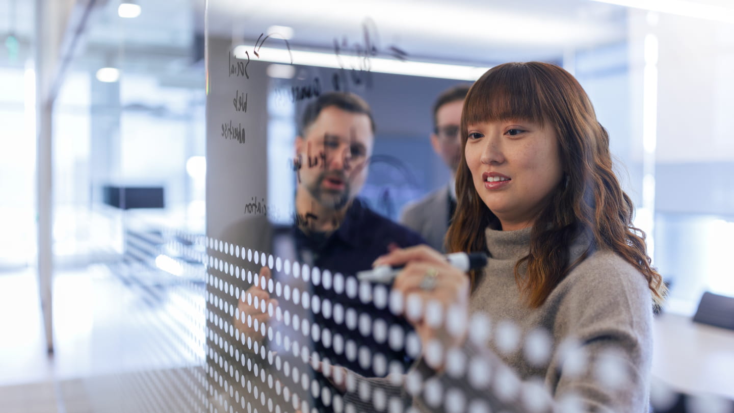 Exact Sciences employees using dry erase markers to write on a glass wall while collaborating in an Exact Sciences office.